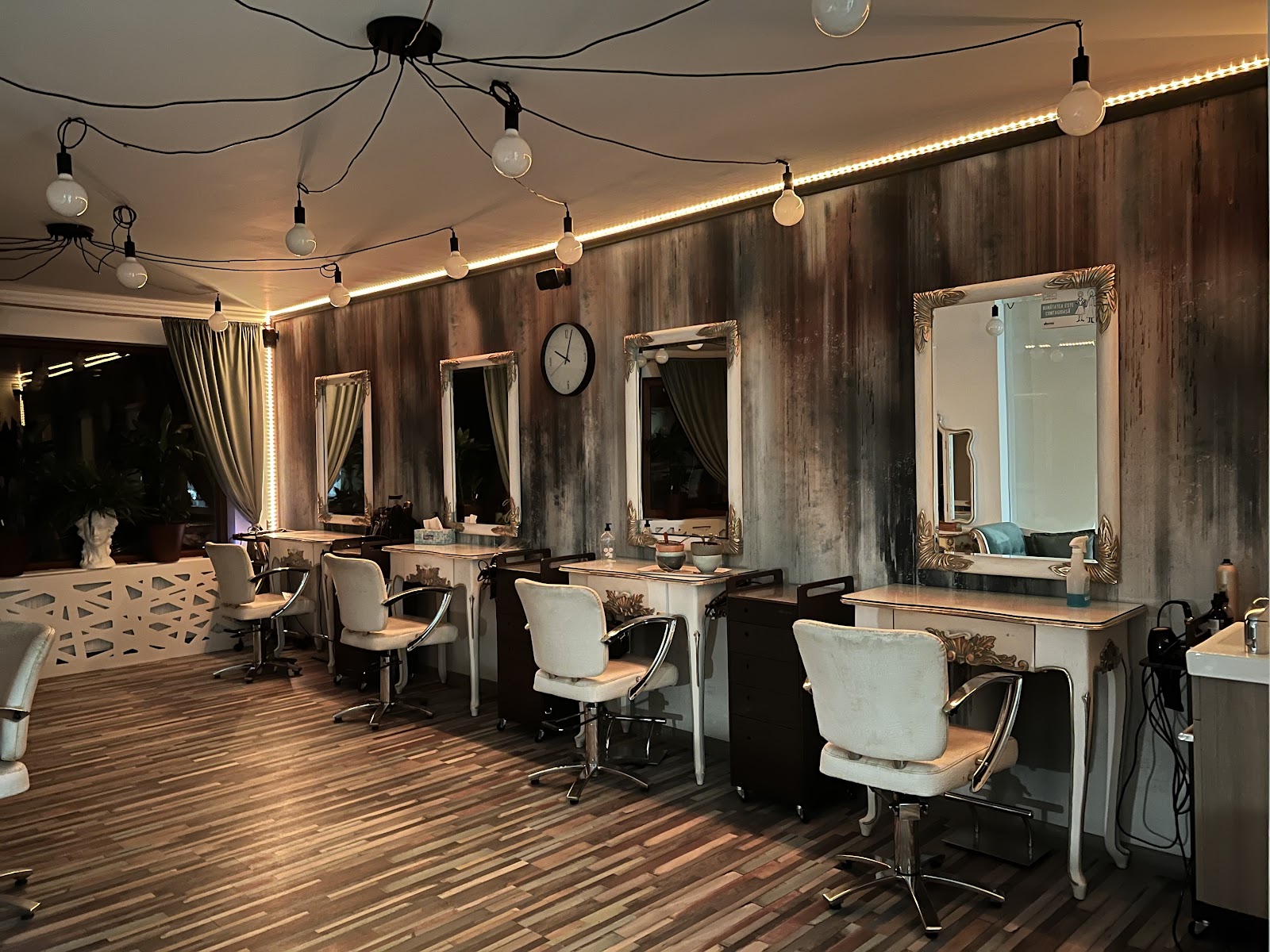 Salonul Beauty Garden seara: console aurite, oglinzi cu rame sculptate, becuri pe cablu negru și peretele cu patină
