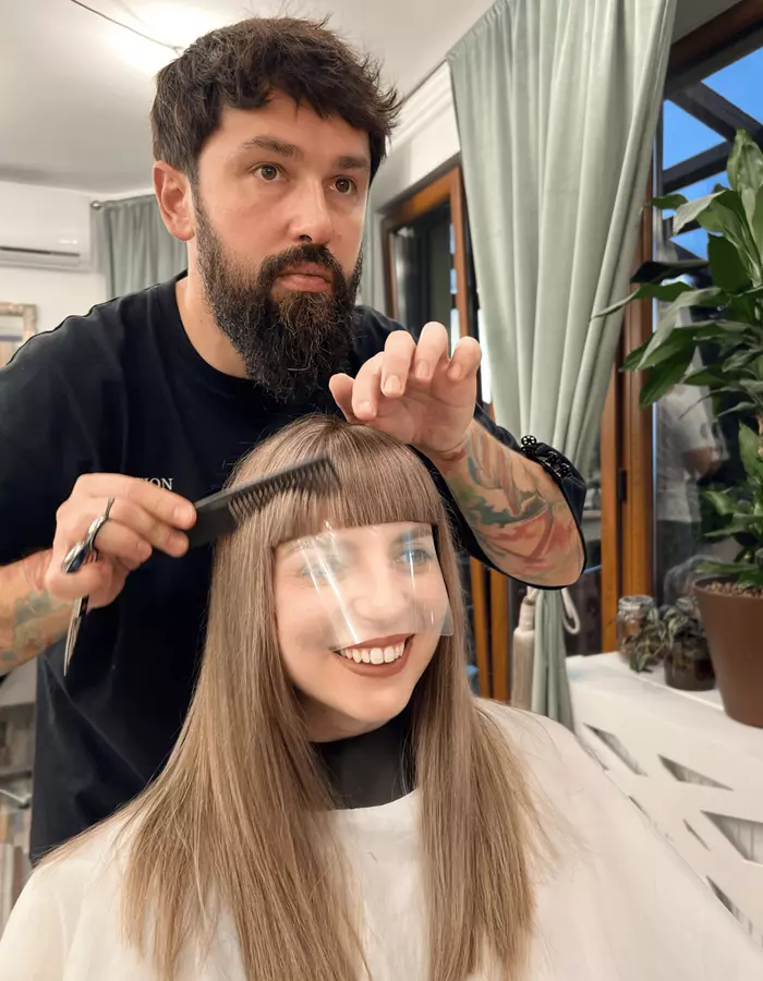 Eduard tunde bretonul unei cliente, lângă fereastra cu plante și draperii verzi